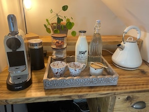Una mesa de madera con una cafetera, una planta, una botella, una tetera y una bandeja con tazas y una cuchara.