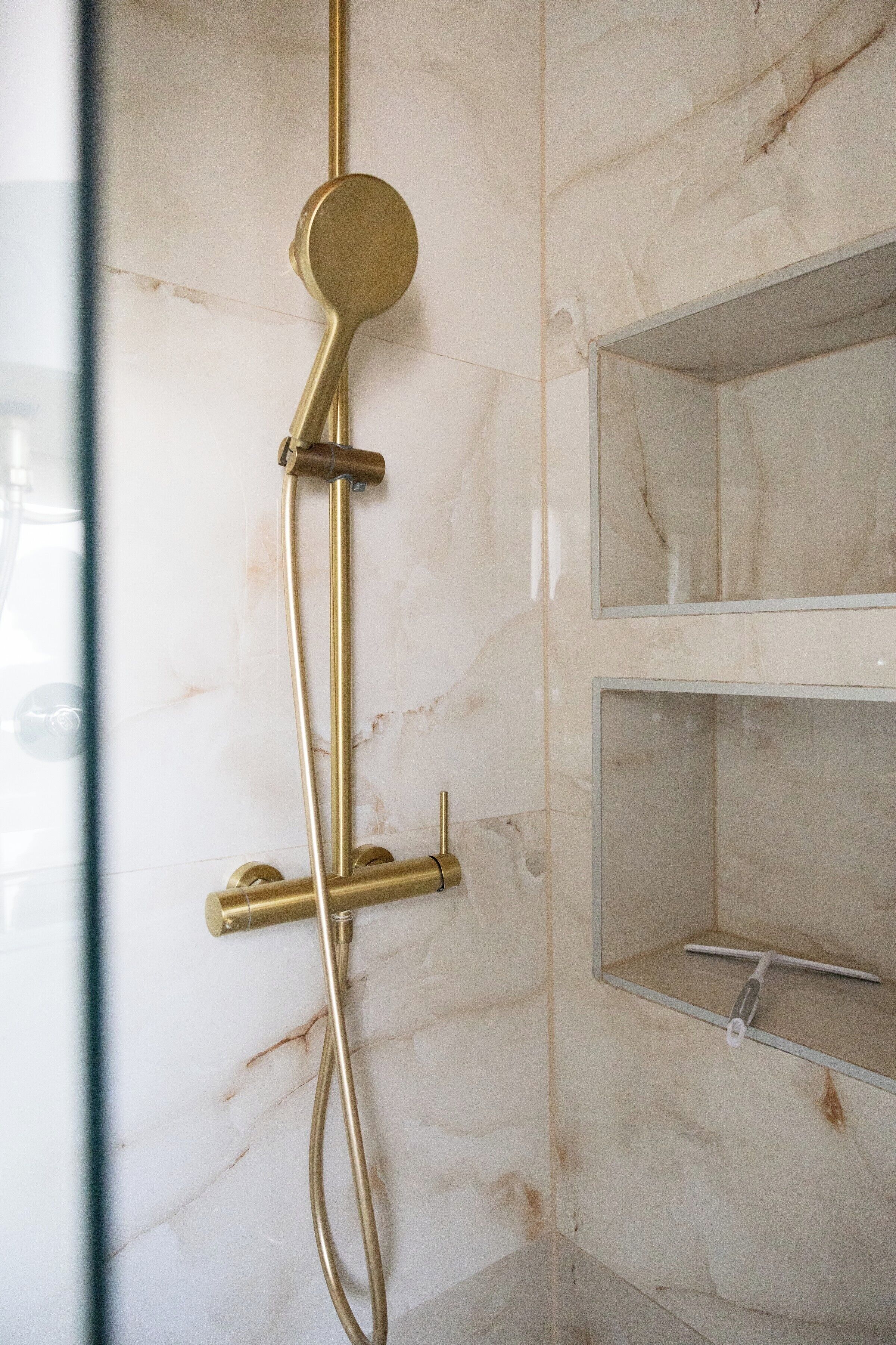 Une salle de bain avec un mur en marbre, une pomme de douche dorée et une paroi de douche en verre.