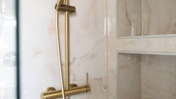 Une salle de bain avec un mur en marbre, une pomme de douche dorée et une paroi de douche en verre.