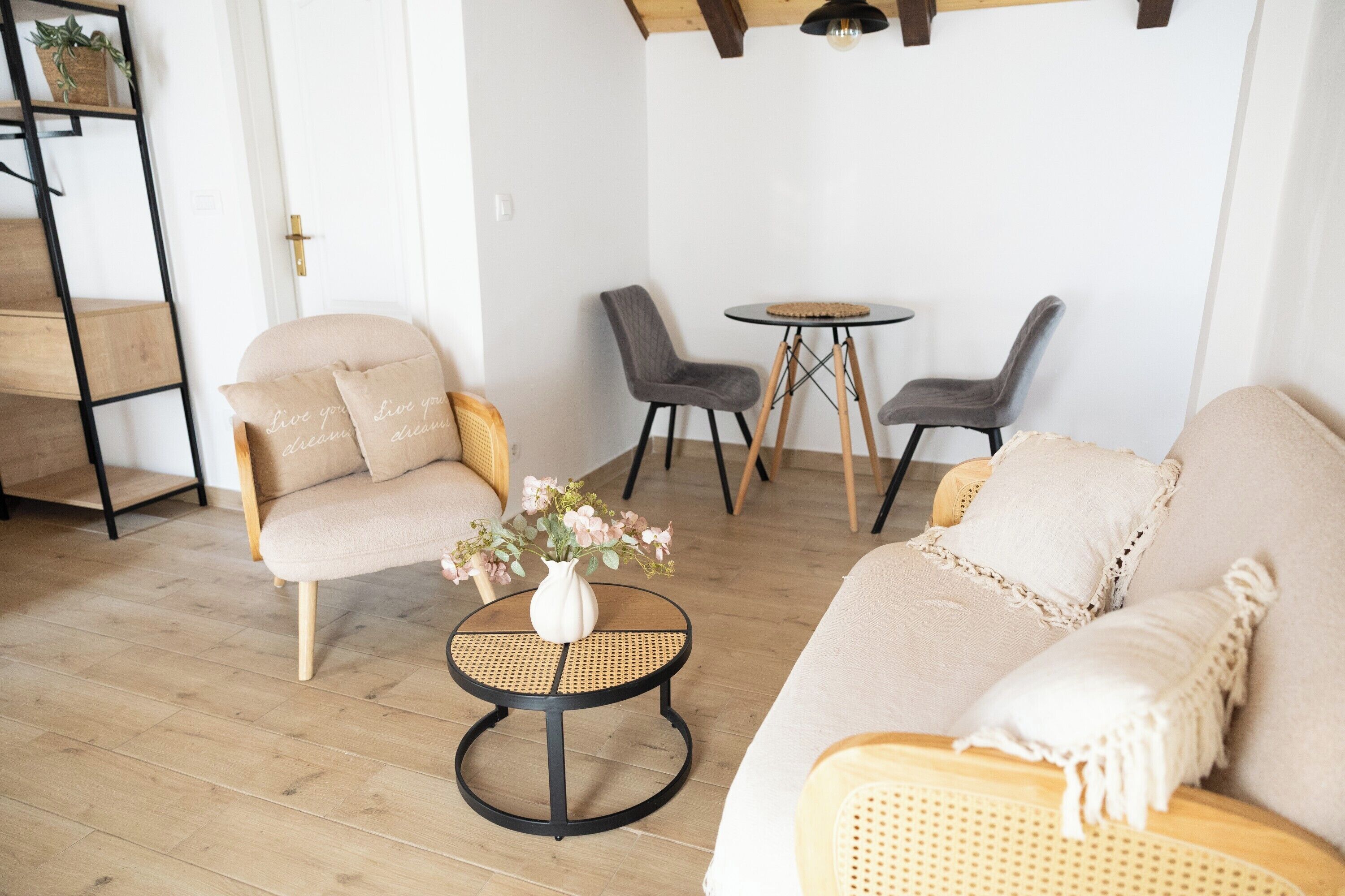 Ett vardagsrum med en soffa, två fåtöljer, ett litet runt bord med en vas med blommor och ett trägolv.