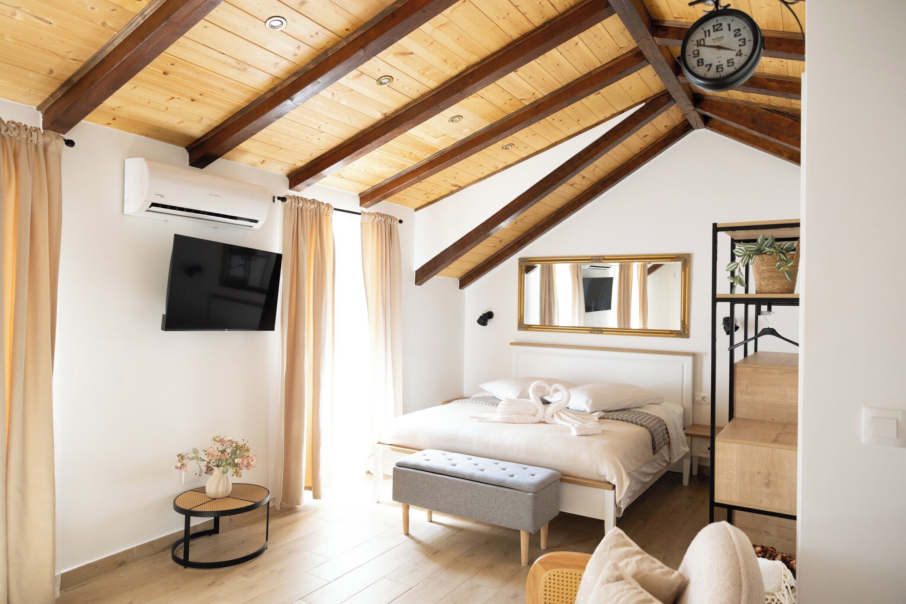 A bedroom with a sloped ceiling, a bed, a bedside table, a mirror, and a wall-mounted TV.