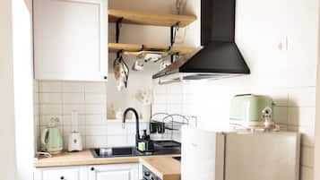 Une cuisine compacte avec des meubles blancs, un plan de travail en bois, une hotte noire et un petit réfrigérateur.