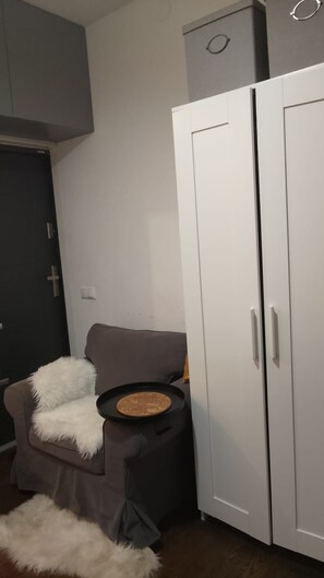 A room with a grey sofa, a small round table with a plate, a white wardrobe, and a dark door. - Studio Sleeps 1 in Sundbyberg (Sundbyberg)