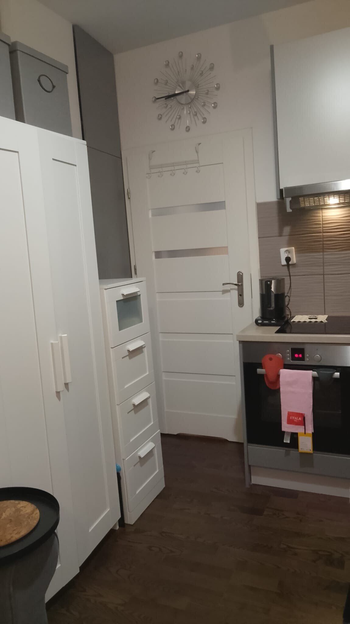 Een keuken met een witte deur, een klok, een fornuis en een koffiezetapparaat.