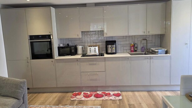 A modern kitchen with white cabinets, a built-in oven, a microwave, a coffee maker, and a sink.