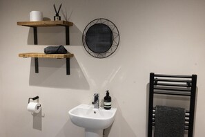 Een badkamer met een witte wastafel, toiletpapier, een handdoekhouder en een decoratief wandobject.