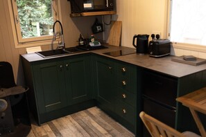 Een keuken met donkergroene kastjes, een spoelbak, een magnetron en een koffiezetapparaat.