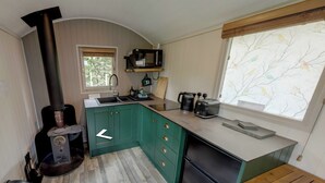 Een compacte keuken met een houtkachel, een wastafel en een raam met uitzicht op bomen.