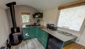 A compact kitchen with a wood stove, a sink, and a window with a view of trees. - Shepherd's Hut - Sleeps 2 - Hot Tub (Northwich)