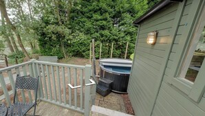 Een houten terras met een metalen stoel, een jacuzzi en een schuur met een lamp.