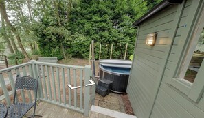 A wooden deck with a metal chair, a hot tub, and a shed with a light fixture. - Shepherd's Hut - Sleeps 2 - Hot Tub (Northwich)