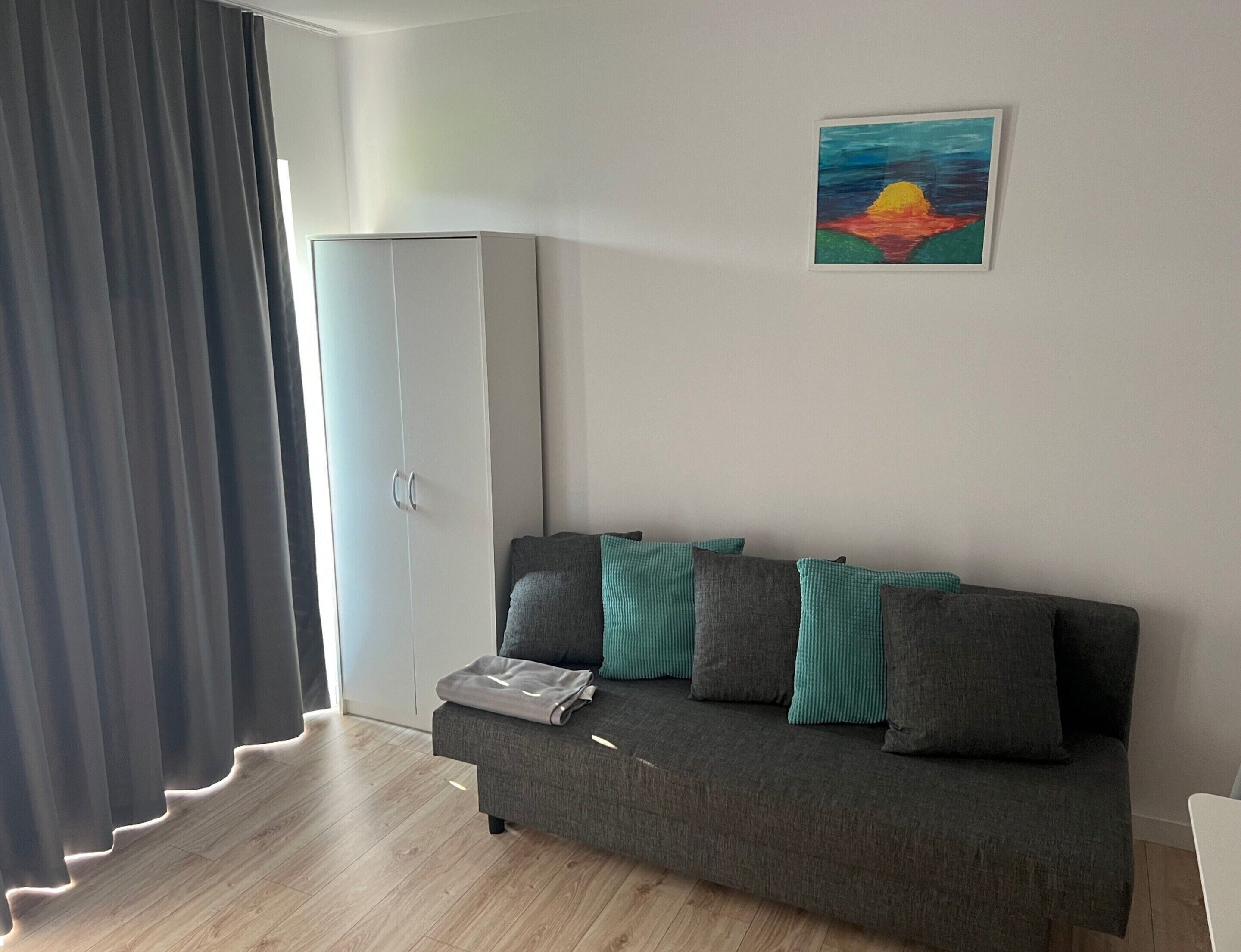 Un salon moderne avec un canapé gris, des coussins turquoise, un tableau au mur et une armoire.