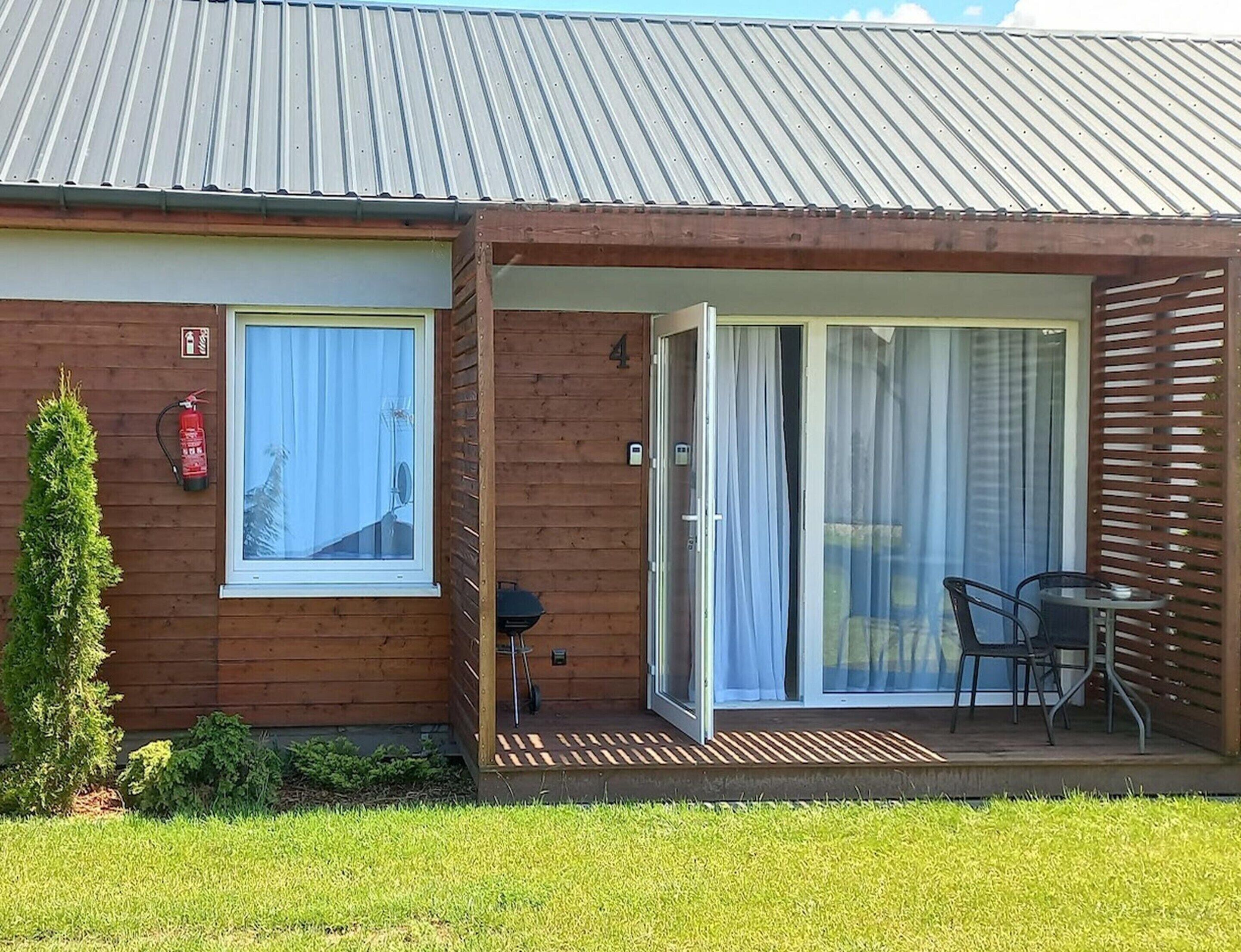 A wooden building with a sliding glass door leading to an outdoor seating area with chairs and a table.