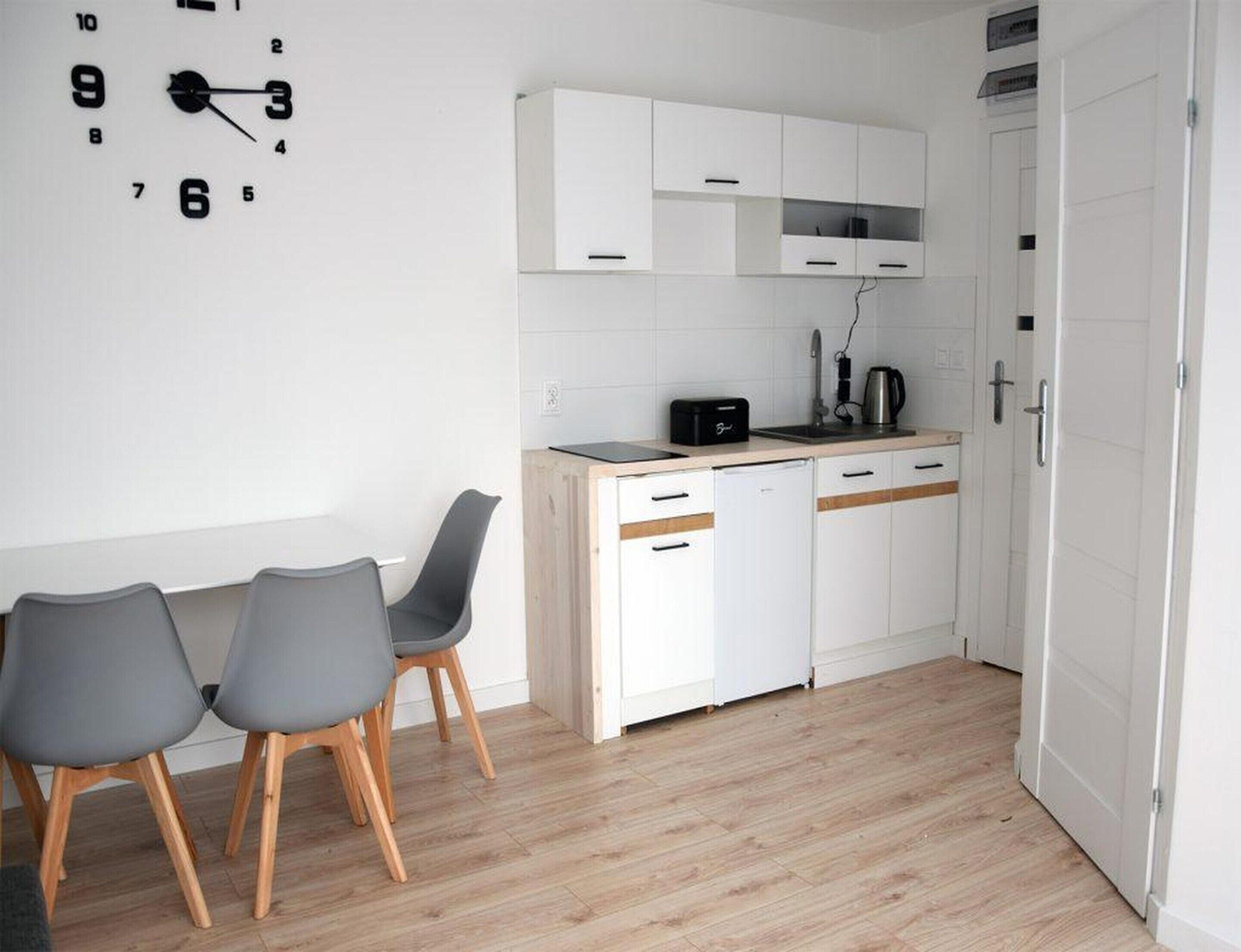Una cocina compacta con armarios blancos, una encimera y un comedor con dos sillas.