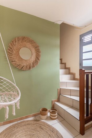 A staircase with a wooden railing, a hanging macrame chair, and a woven wall hanging. - Apartement Bèt a Fé, Les Trois-Ilets (Les Trois-Îlets)