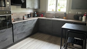 Moderni keittiö, jossa on tummat kaapit, ruostumattomasta teräksestä valmistettu liesi, ikkuna, josta avautuu näkymä vehreään maisemaan, ja baarituoli.
