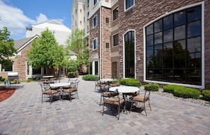 Un patio con mesas al aire libre, un edificio de piedra y un ventanal grande.
