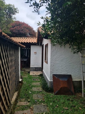 A narrow stone pathway leading to a white building with a tiled roof, surrounded by greenery and a wooden fence. - Casa Lírio  (Teresópolis)