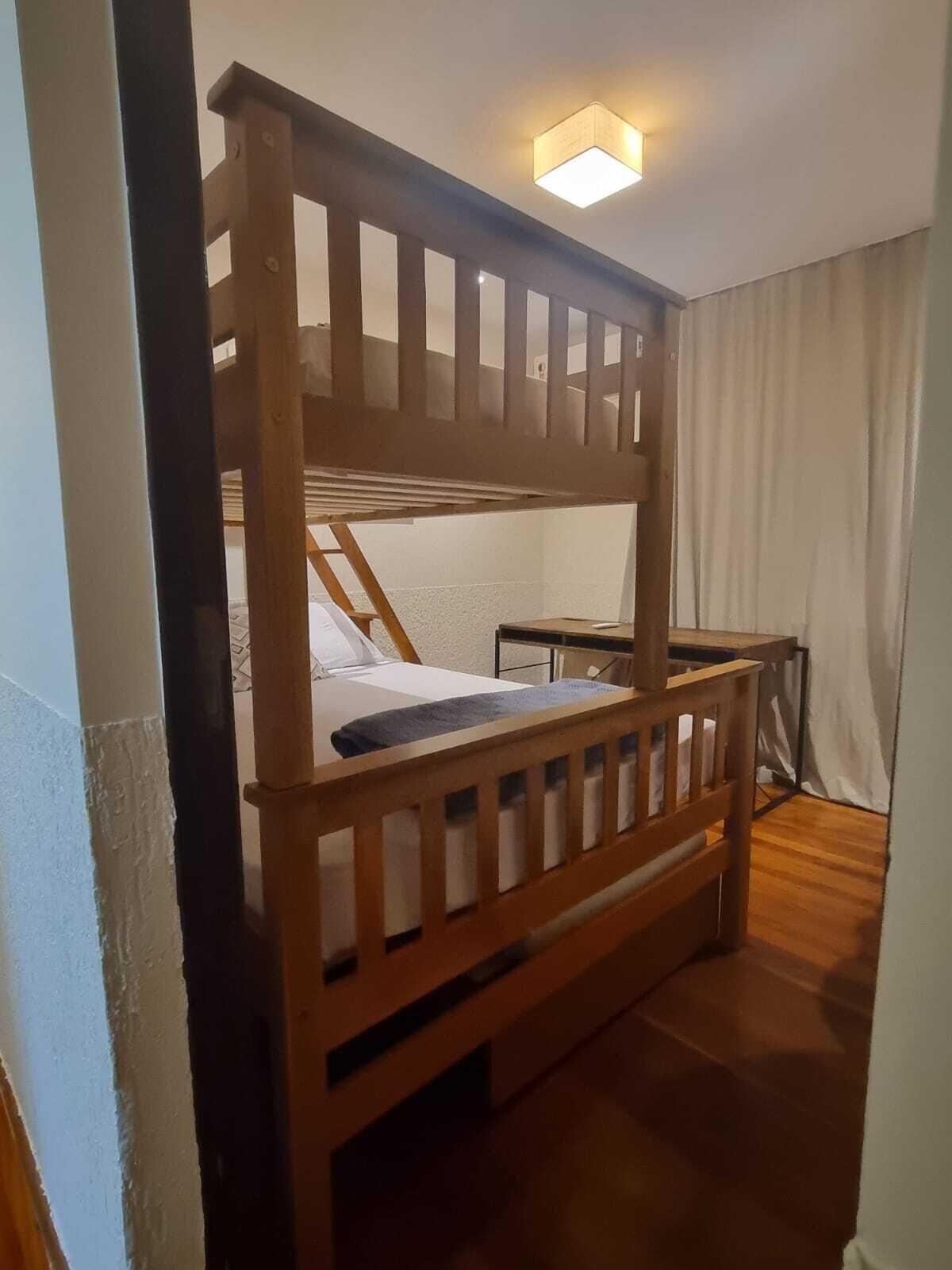 Una cama individual sobre otra, con estructura de madera, una mesita de noche y una mesilla.