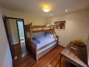 A bunk bed room with a wooden floor, a desk with a chair, a painting on the wall, and a door leading to another room. - Casa Lírio (Teresópolis)
