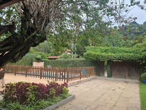 A courtyard with a wooden fence, a stone pathway, and lush greenery. - Casa Lírio  (Teresópolis)