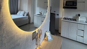 Een moderne hotelkamer met een ronde spiegel, een bed, een kitchenette en een eethoek.