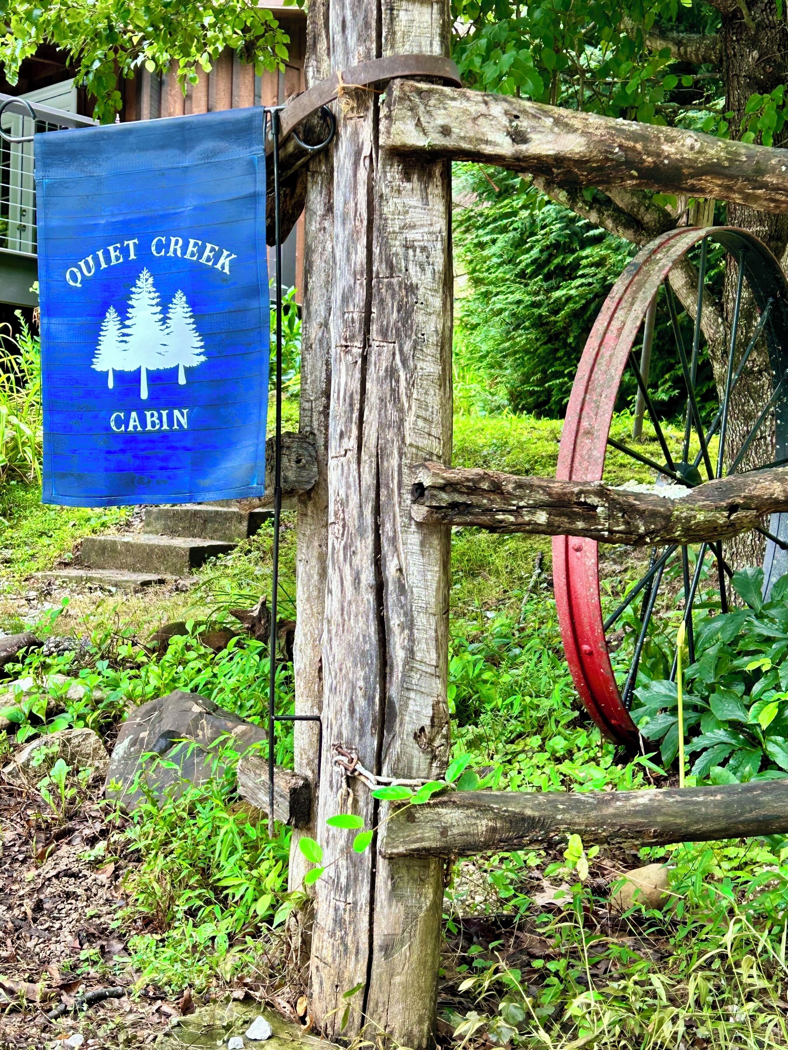 Placa rústica de cabana com uma floresta e uma roda d'água.
