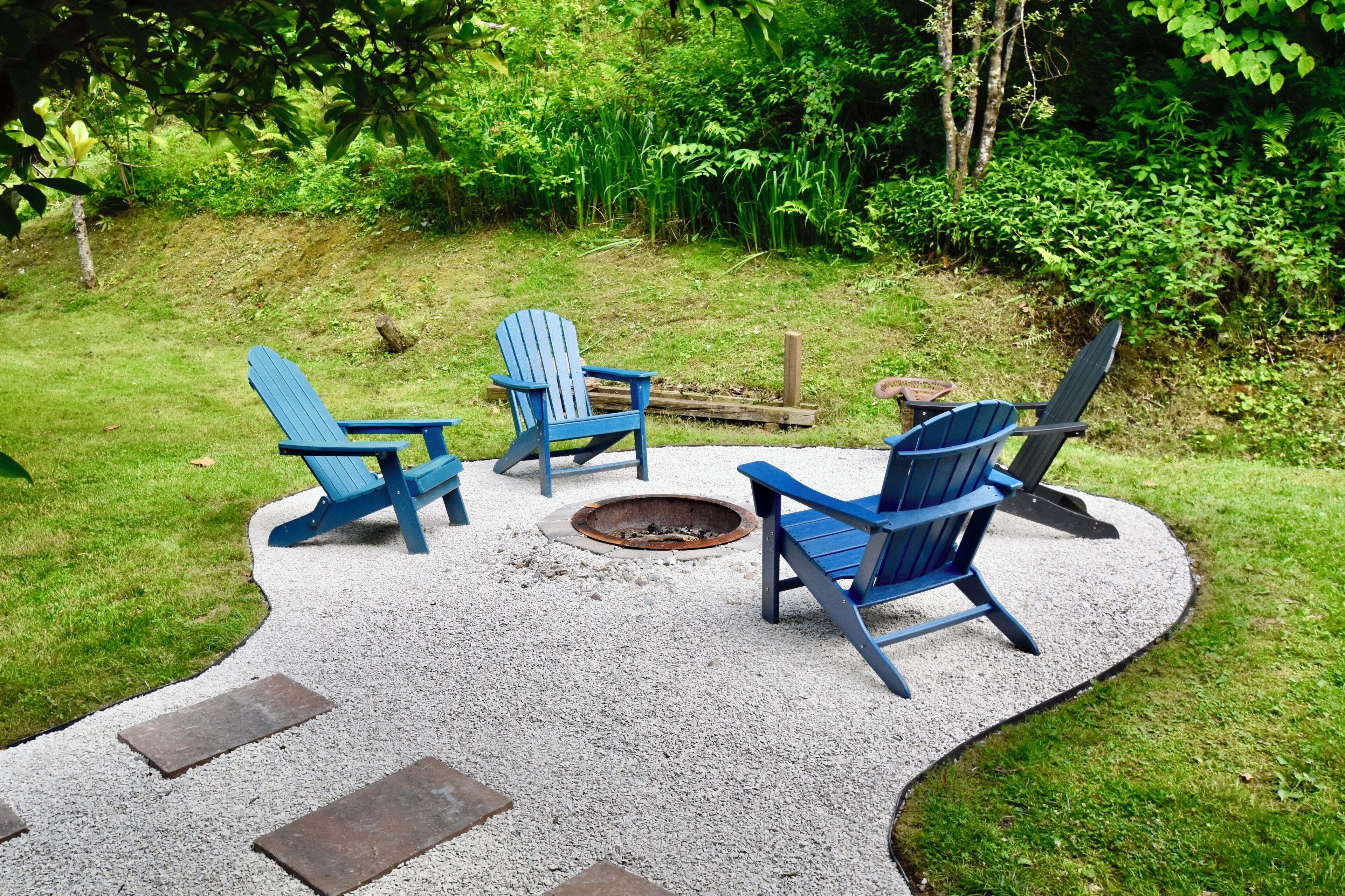 Un espace patio aménagé avec trois fauteuils Adirondack disposés autour d’un foyer.