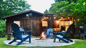 Une cabane rustique avec un foyer et des fauteuils Adirondack dans la cour.
