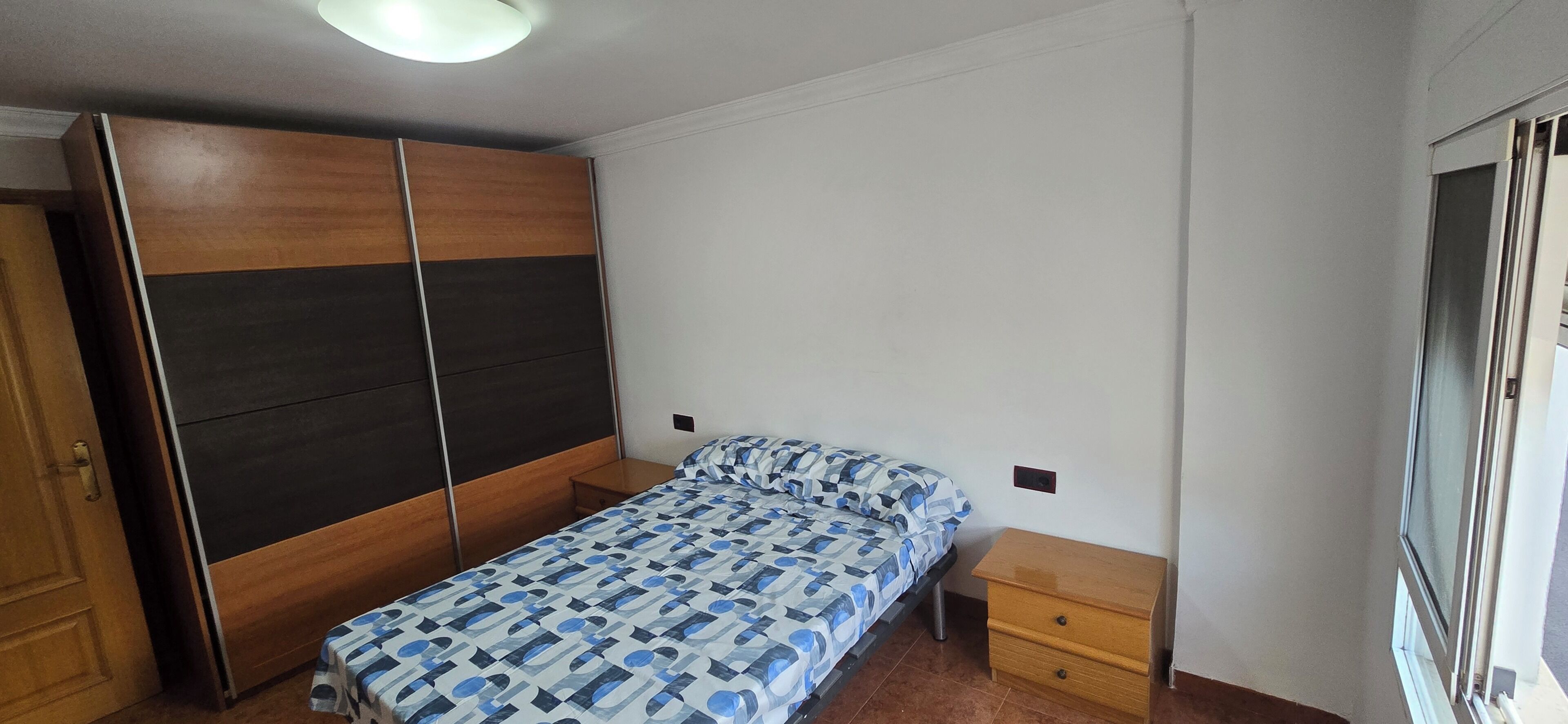 Une chambre à coucher avec un lit, une armoire en bois, une table de chevet et une fenêtre.