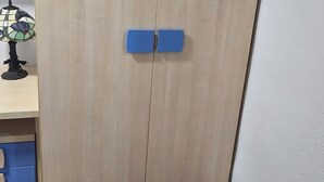 Ett rum med en garderob i trä, en blå stol och ett litet bord med en dekorativ prydnad.