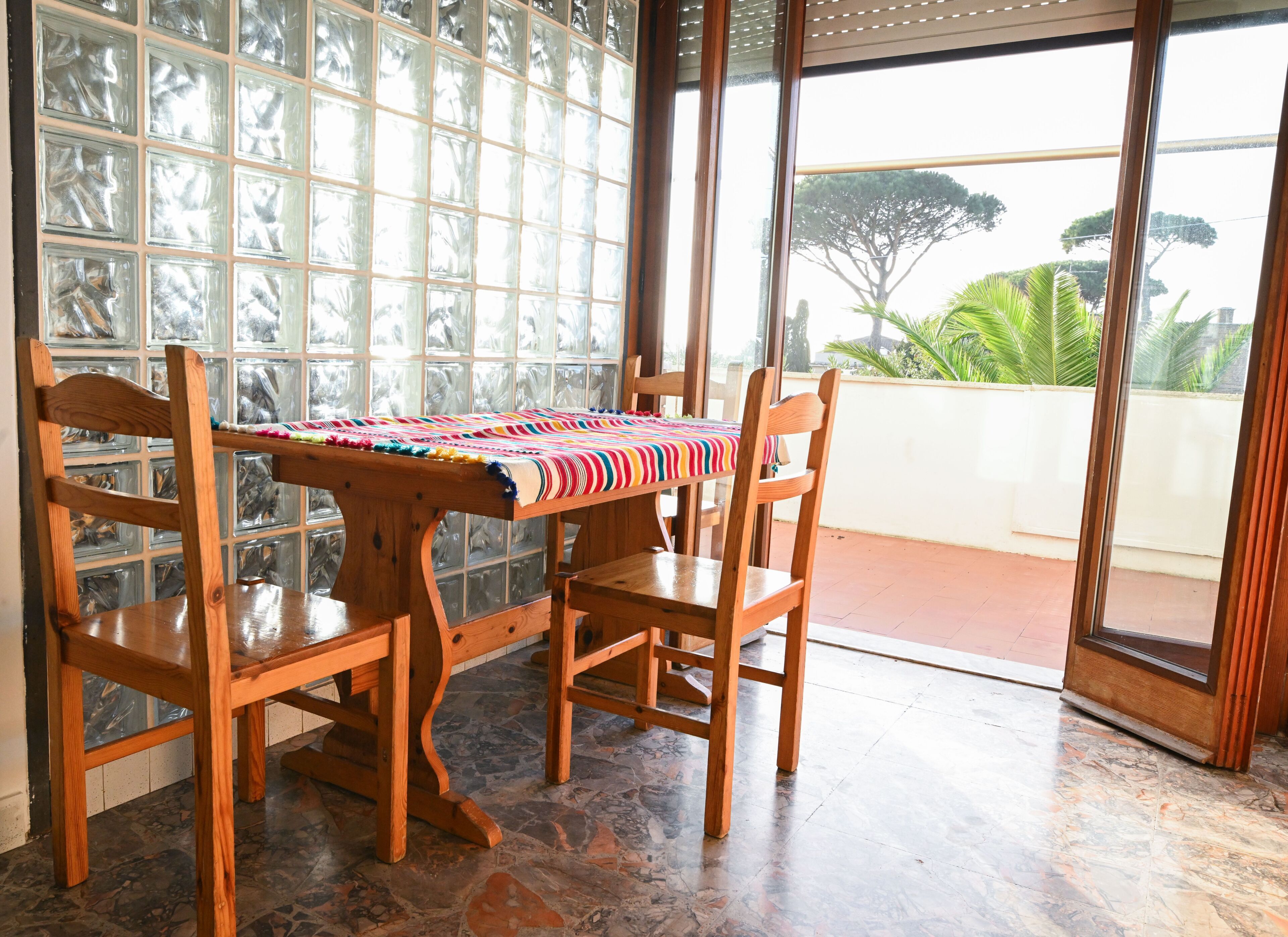 Una habitación con una mesa y sillas de madera, un mantel estampado y vistas amplias a través de grandes ventanales.