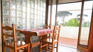 Una habitación con una mesa y sillas de madera, un mantel estampado y vistas amplias a través de grandes ventanales.