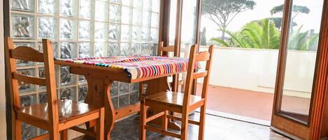 Una habitación con una mesa y sillas de madera, un mantel estampado y vistas amplias a través de grandes ventanales.