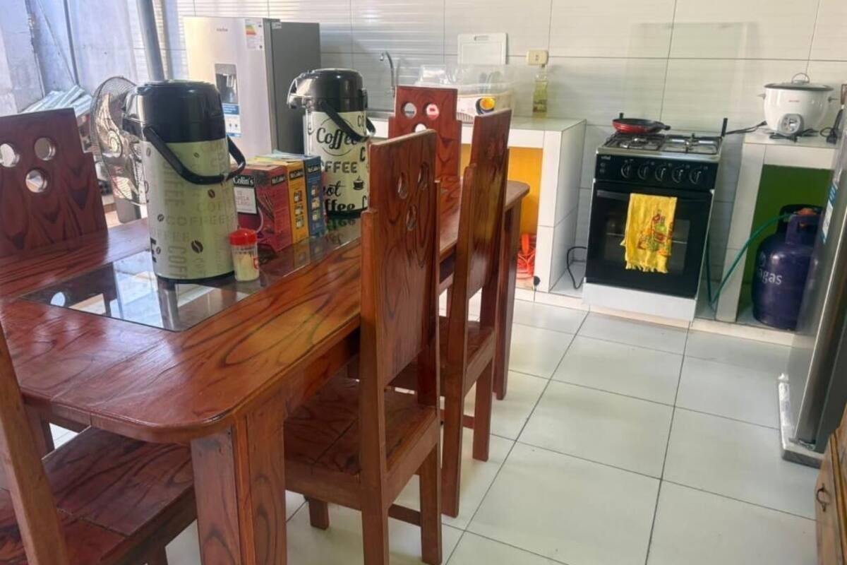 Una cocina con una mesa de comedor y sillas, una cafetera, una estufa y un cilindro de gas.