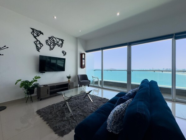 Una sala de estar moderna con un televisor grande, un sofá, una mesa de centro y vistas al mar.