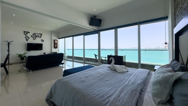 Une chambre moderne avec un grand lit, une télévision, un balcon avec vue sur la mer et un bureau avec une chaise.