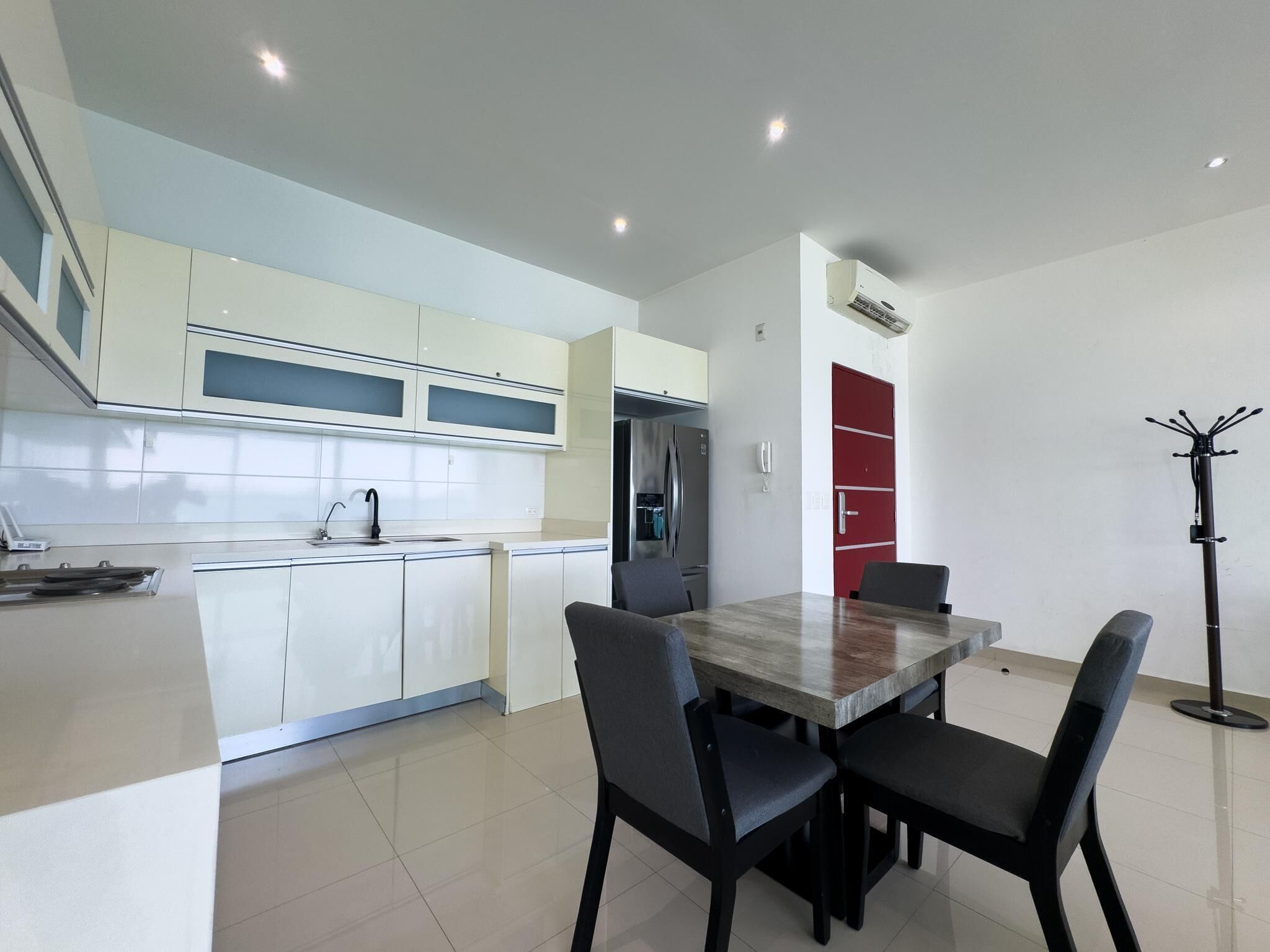 Une cuisine moderne avec des meubles blancs, une table à manger et quatre chaises, et une porte rouge.