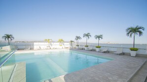 Une piscine sur le toit, avec une eau d’un bleu cristallin, entourée de chaises longues et de palmiers.