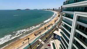 Un paysage urbain côtier avec une plage, une route parallèle au rivage et des immeubles modernes dotés de balcons.