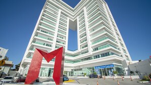 A modern high-rise hotel with a distinctive red arrow sculpture in front. - Beautiful Malecon and Beyond 514 Torre eMe (Mazatlán)