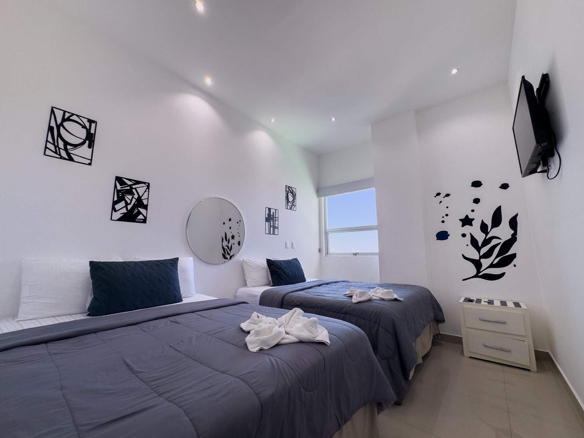 Una habitación de hotel moderna con dos camas, un espejo grande, obras de arte en las paredes, un televisor y una ventana.