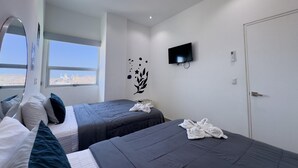 A hotel room with two beds, a TV, a window with a city view, and a door. - Beautiful Malecon and Beyond 514 Torre eMe (Mazatlán)