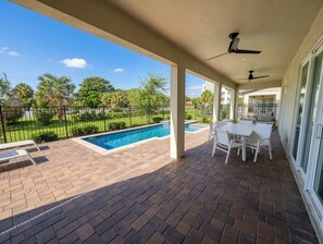 Eine überdachte Terrasse mit Pool, Sitzgelegenheiten im Freien und Blick auf die umliegende Bepflanzung.