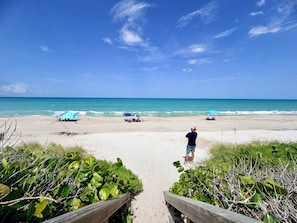 A beach with a wooden walkway leading to the shore, umbrellas, and people relaxing. - Heated Pool/Spa (included), Theater, Game Room (Melbourne Beach)