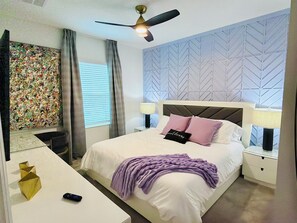 Ein Schlafzimmer mit Bett, Deckenventilator, Nachttisch, Lampe, Schreibtisch mit Fernbedienung und Wanddeko.