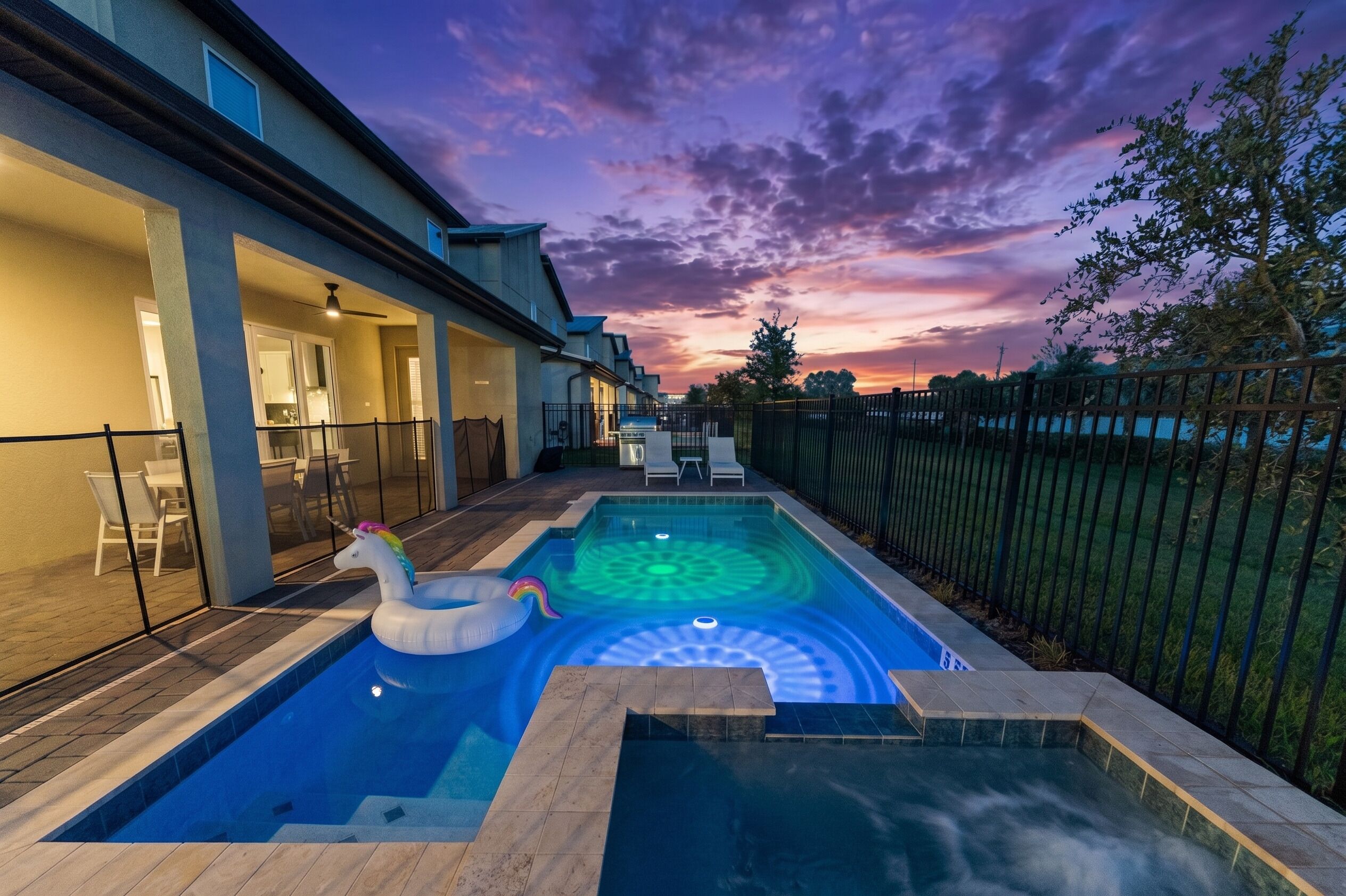 A swimming pool with a unicorn float, a patio area with chairs, and a sunset view.