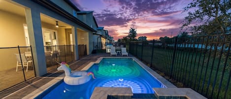 A swimming pool with a unicorn float, a patio area with chairs, and a sunset view.