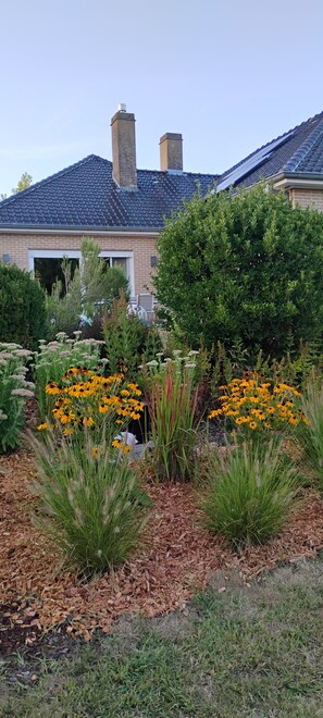 A residential garden with a brick house, a large tree, and vibrant yellow flowers. - Charming vacation home with a terrace and sweeping views of the hills of Ronse (Ronse)