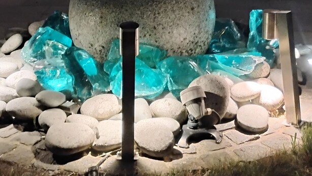 Escultura de piedra en un jardín con muro de ladrillo y puerta de vidrio corredera que da a un espacio interior con muebles.